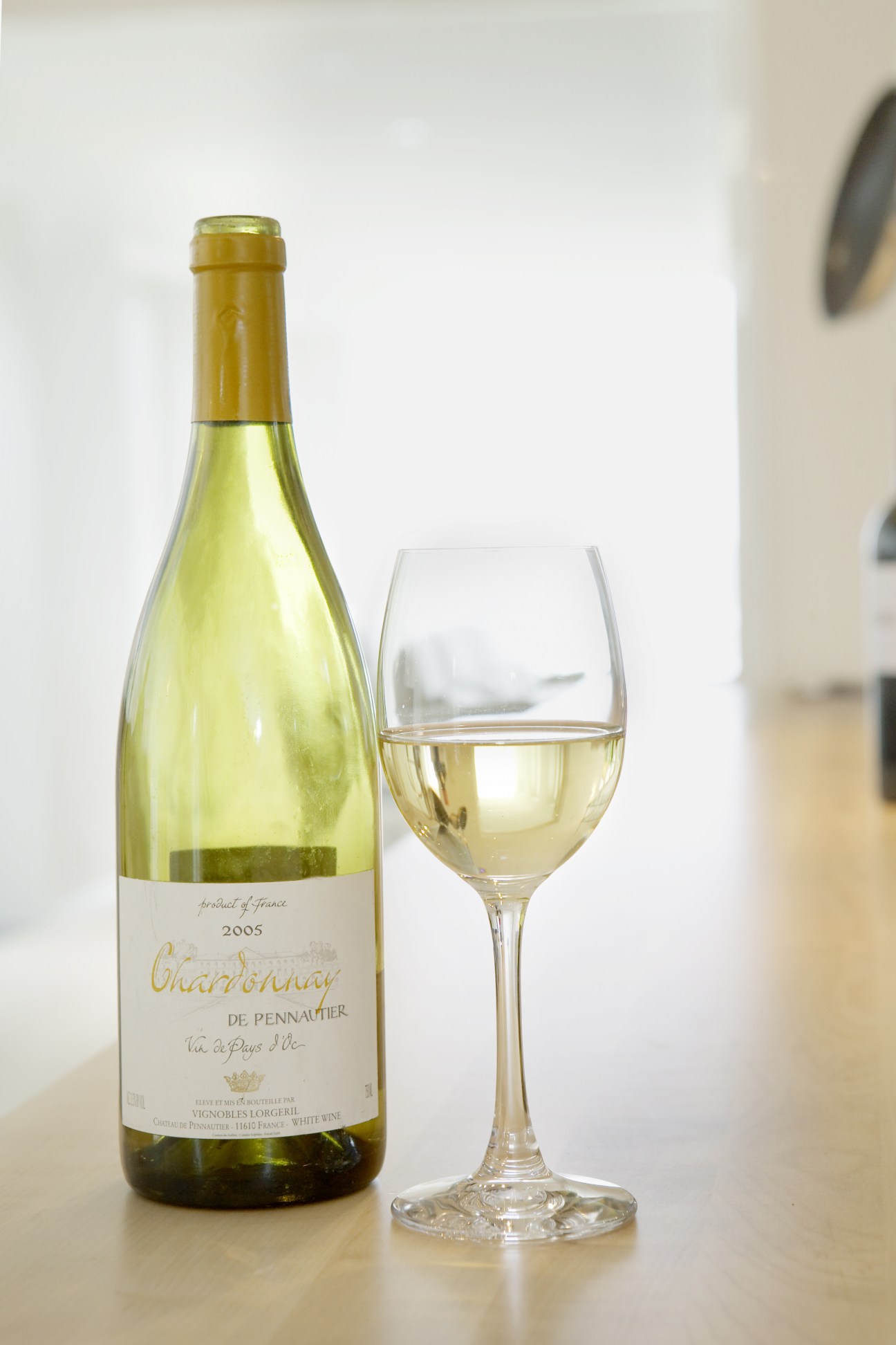 Bottle of French Chardonnay wine next to a filled wine glass on a light surface.