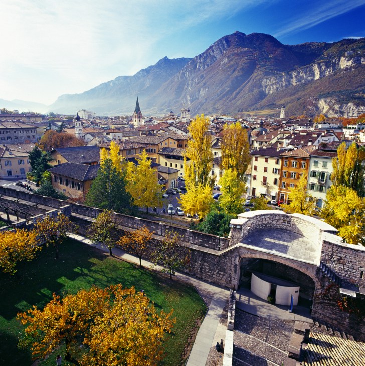 Aerial view of Trento, Italy with autumn foliage, Alpine mountains, churches, and historic architecture.