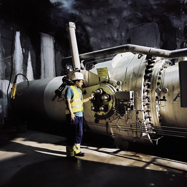 Engineer in safety gear inspecting a large industrial steel turbine at the Khimti hydropower plant.