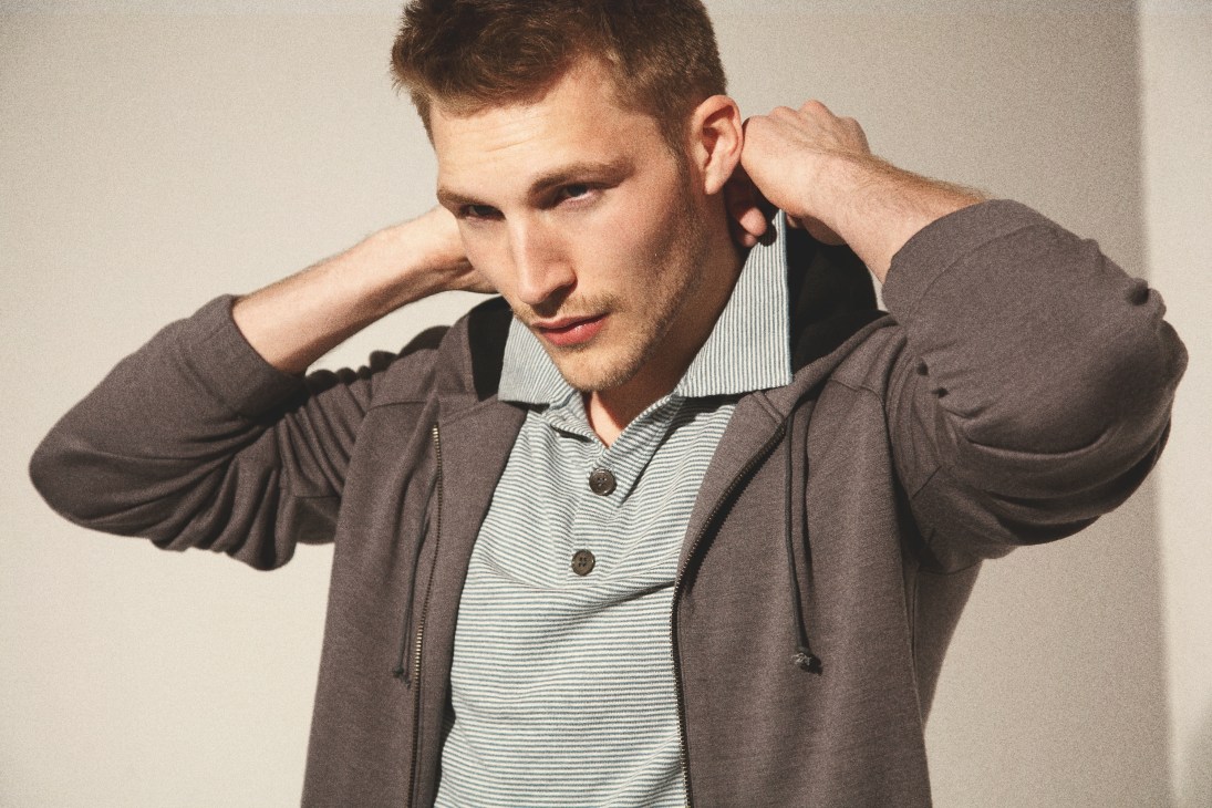 Man wearing Outlier hooded jacket with striped shirt underneath, hands adjusting hood.