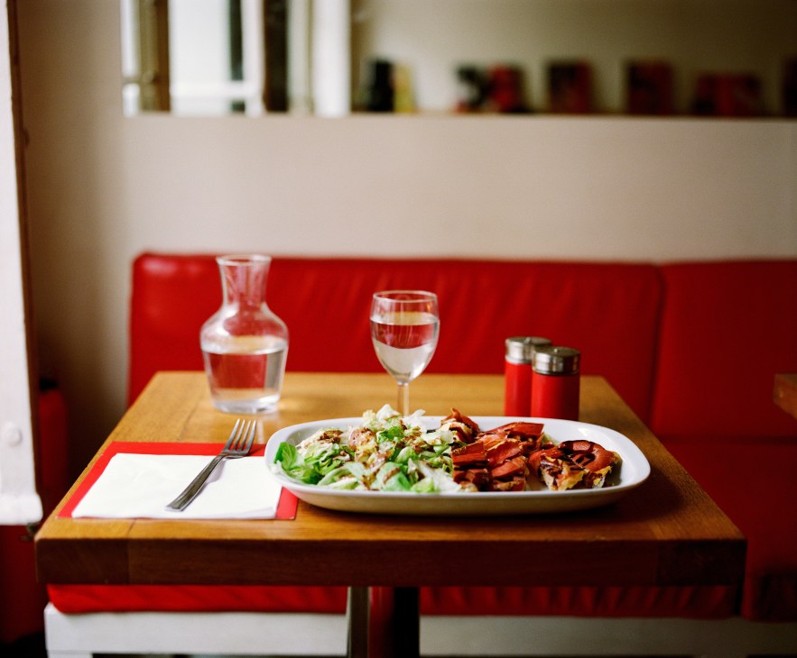 A minimalist dining setup at Simple coffee shop with a plated meal and wine glass against red banquettes.