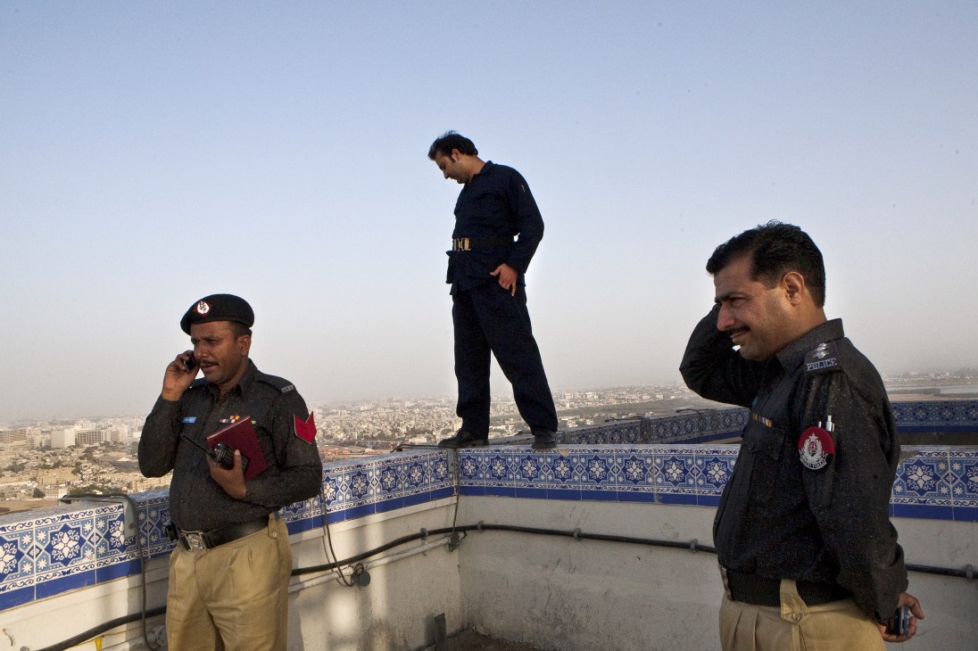 Three police officers stand on the roof of Karachi's Habib Bank Plaza overlooking the city.