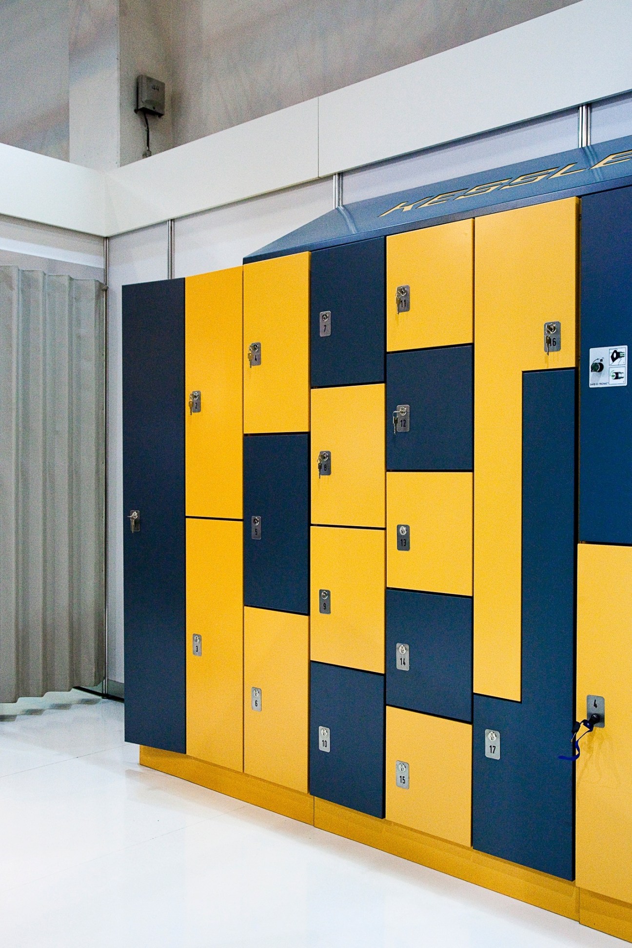 Yellow and navy blue modular lockers by Kessler & Söhne with metal locks and numbered placards.