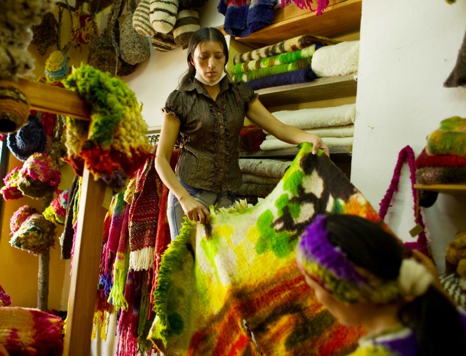Alieth Ortiz stands in her knitware shop surrounded by colorful handcrafted knitted garments and textiles in vibrant hues.