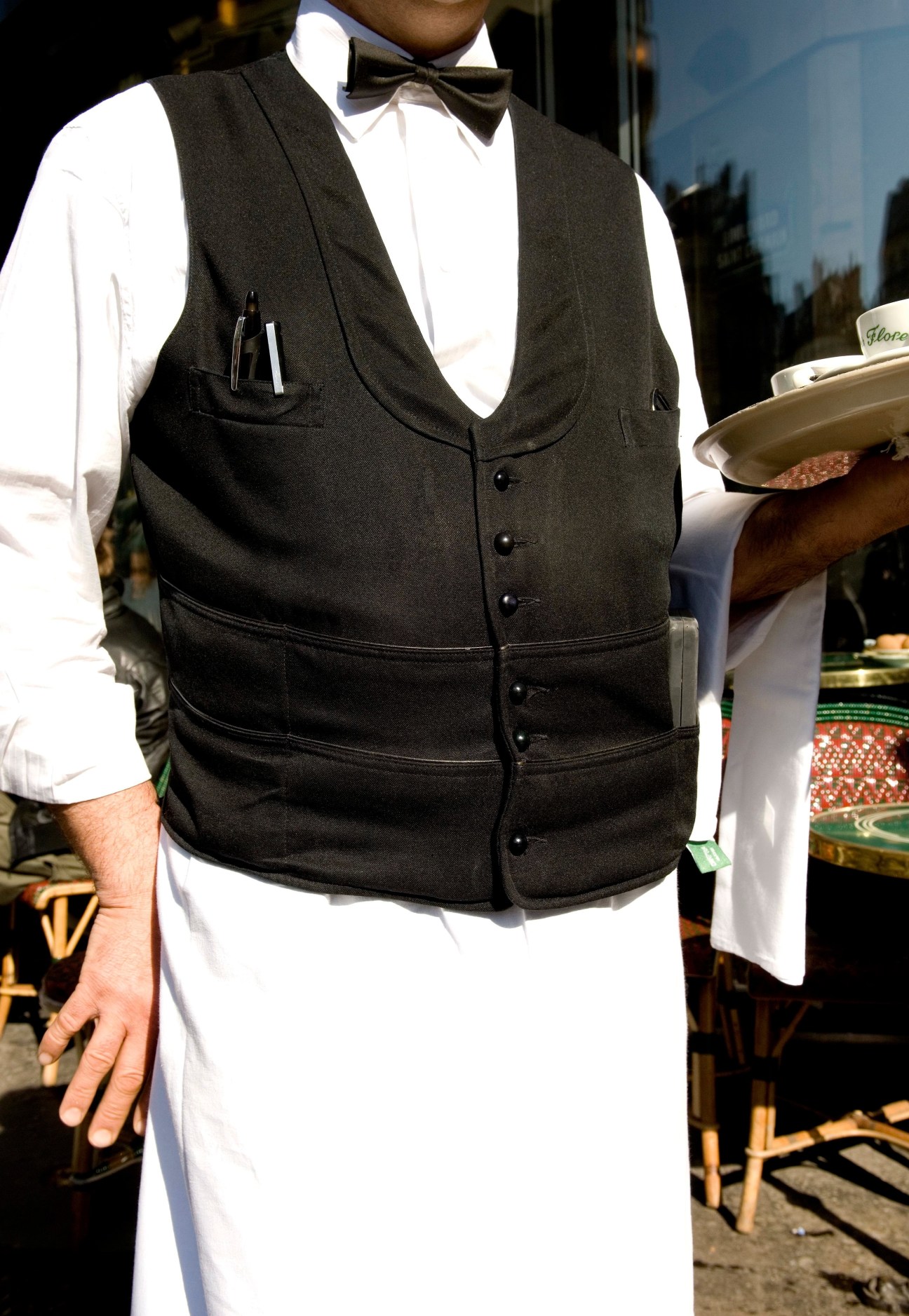 Café de Flore waiter in formal black waistcoat, white shirt, and bow tie serving food.