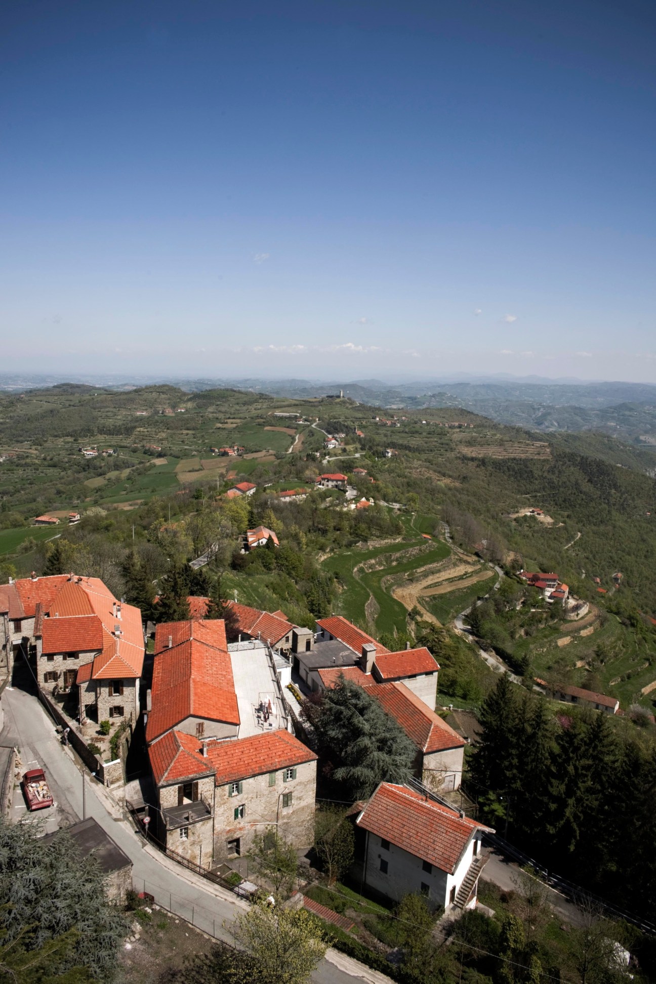 Aerial view of Roccaverano, a medieval Italian town with red-roofed buildings nestled in green rolling hills.