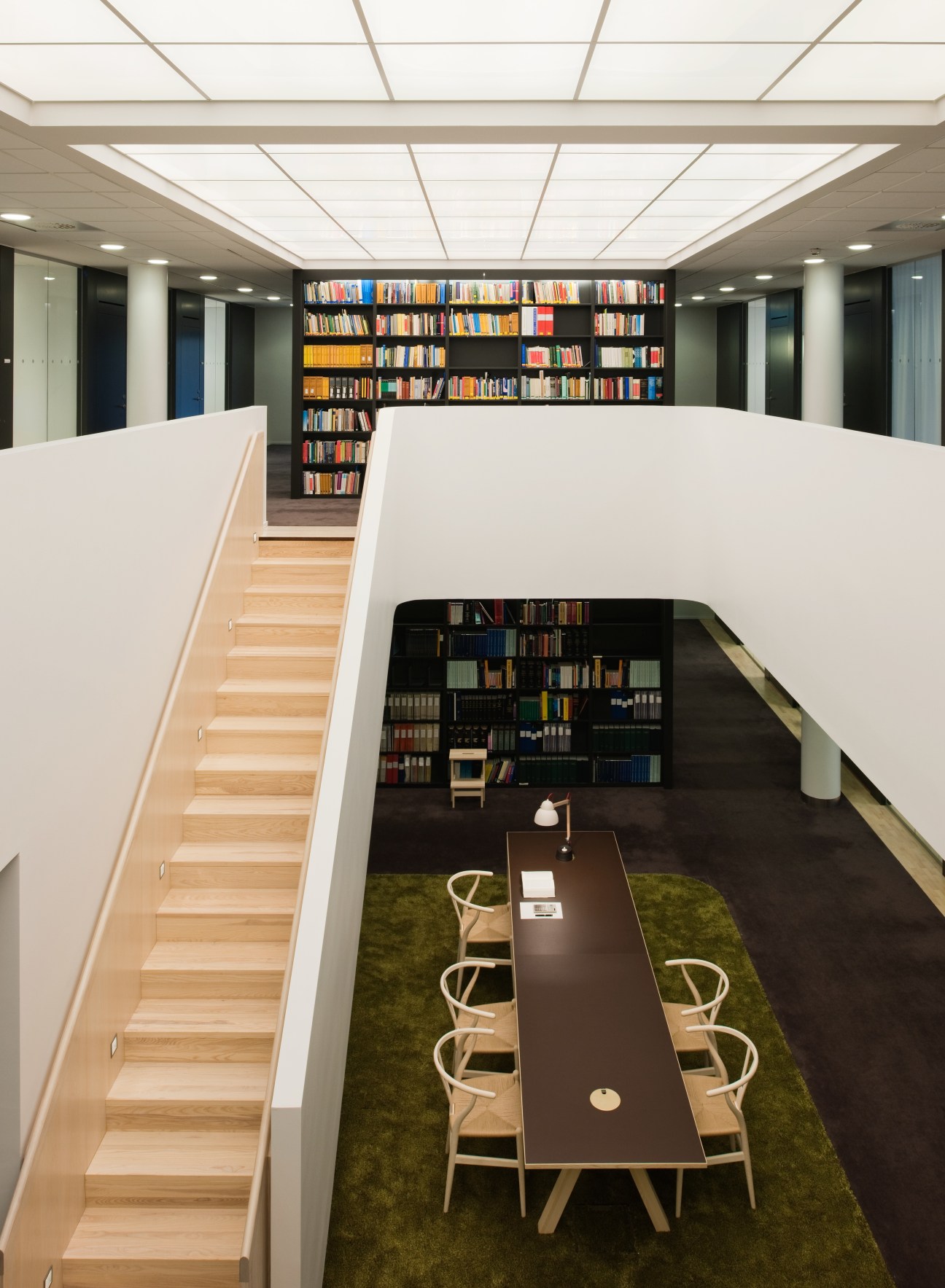 Modern law office library with white gypsum barrier, wooden staircase, and bookshelves across two floors with natural lighting.