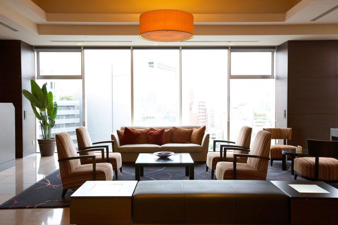 Modern hotel suite lounge with striped armchairs, sofa, orange ceiling fixture and city views.