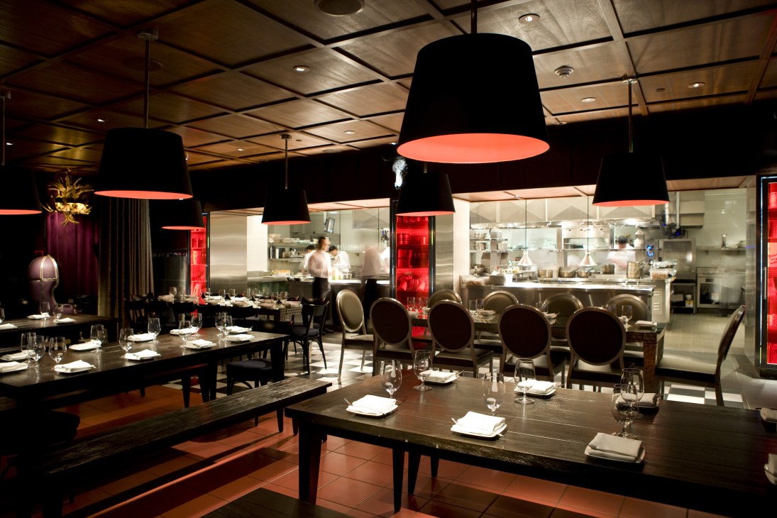 Modern dining room with Philippe Starck-designed black pendant lamps, dark wood tables, and open kitchen visible through glass partition.