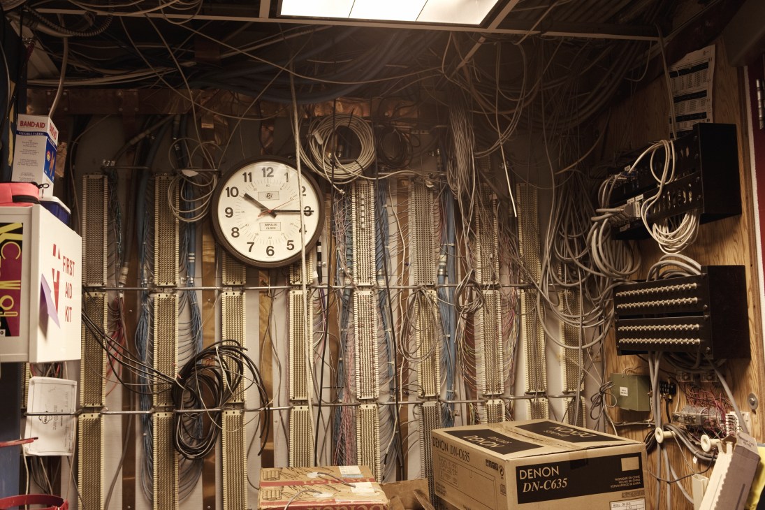 KCRW's music server room with tangled cables, a wall clock, and audio equipment including a Denon DN-C635 unit.