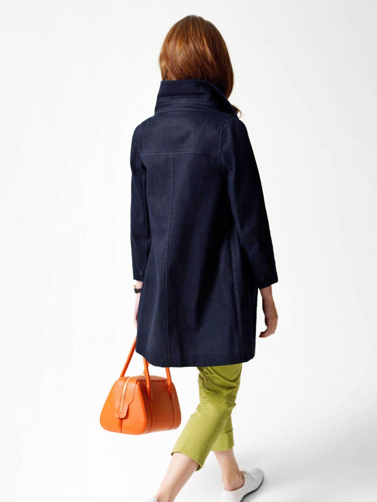 Model wearing navy Prada coat, lime trousers, and carrying an orange Delvaux bag, shown from behind.
