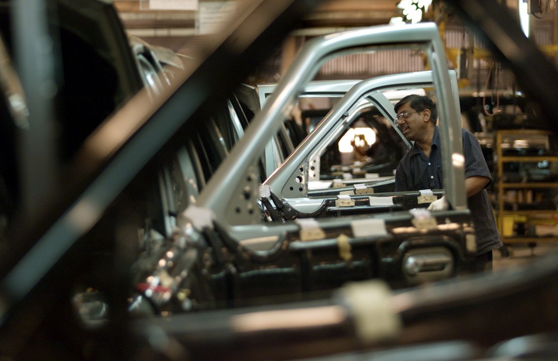 Worker inspecting car door frame at Tata manufacturing plant assembly line.