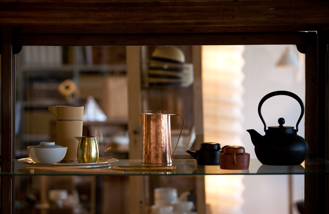 Display of design objects including a black teapot, ceramic bowls, and copper vessels in a shop window.