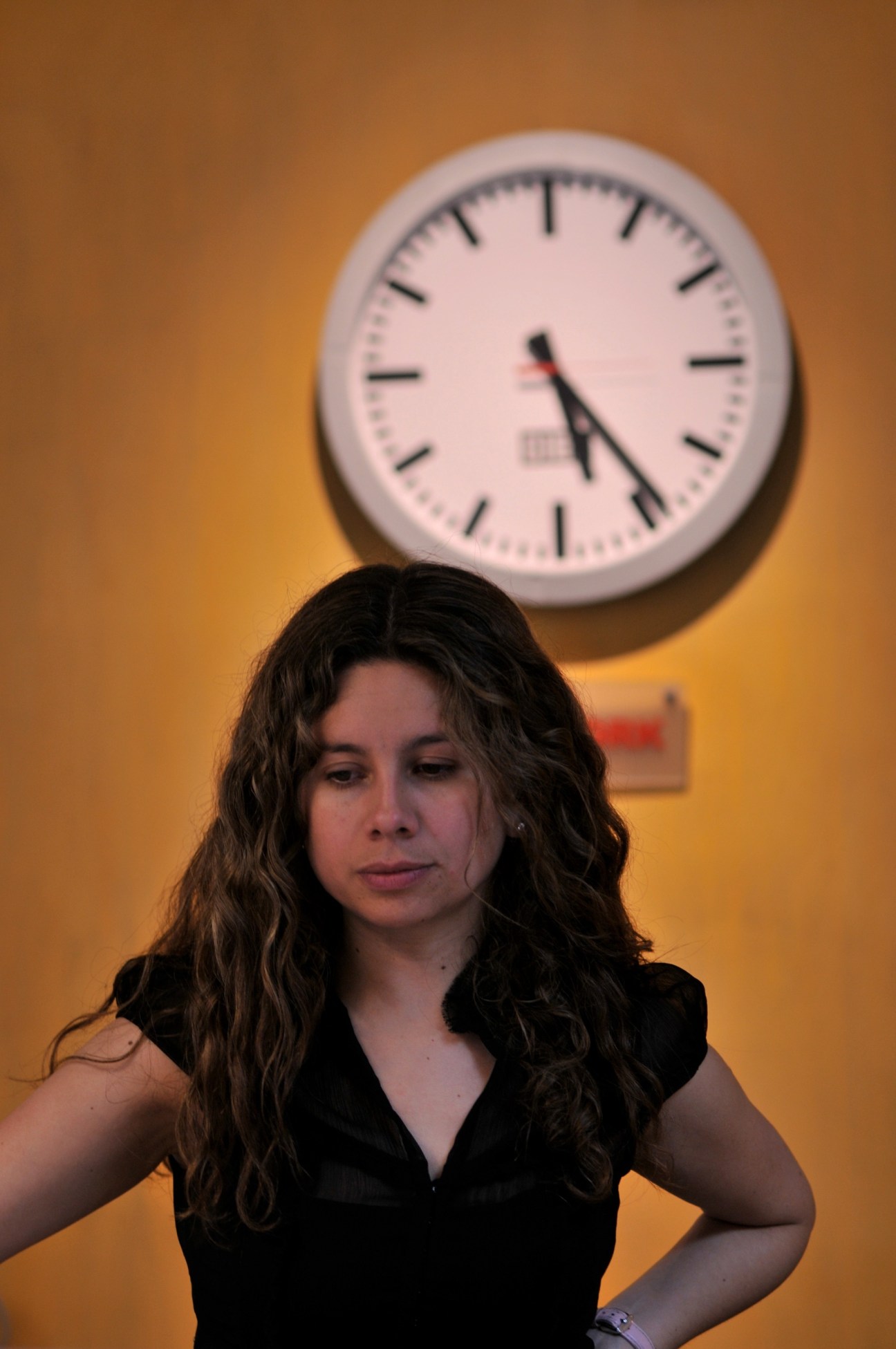 International editor Angelica Lagos standing against a yellow wall beneath a white clock.