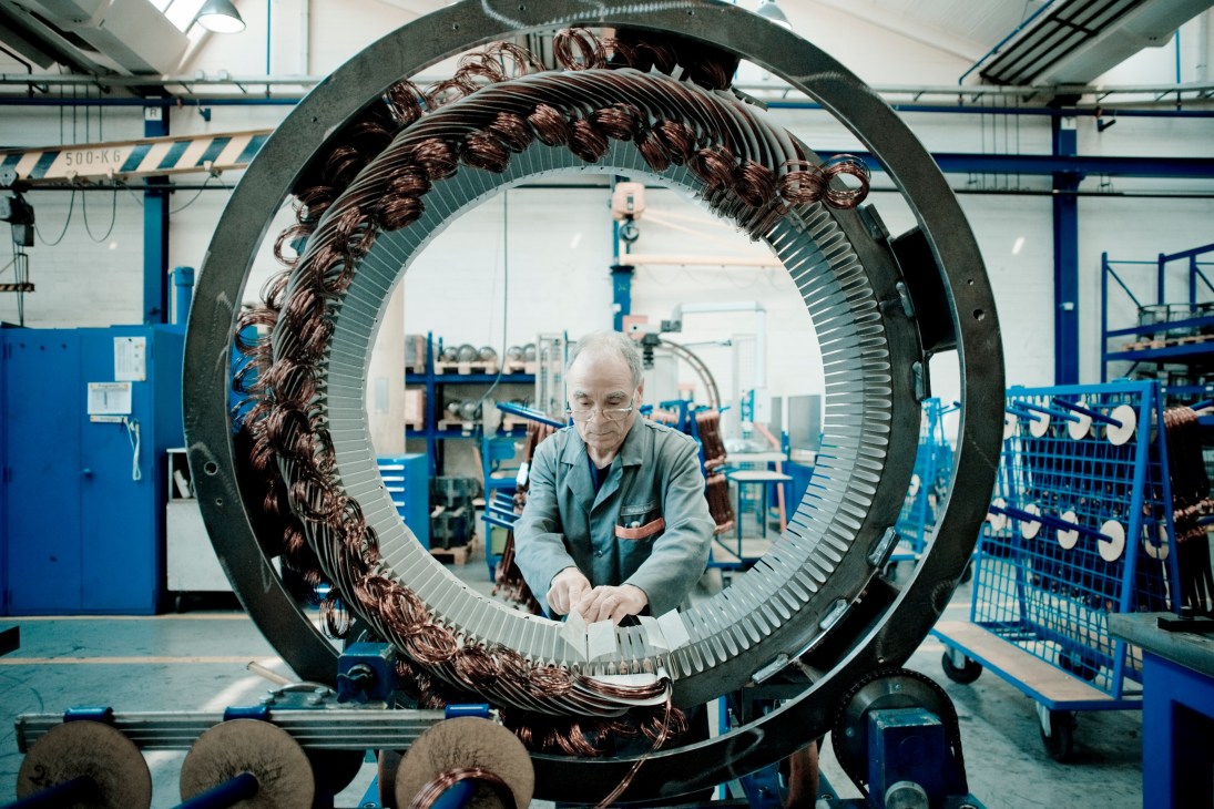 Worker inspects large circular motor component with copper windings at Schindler factory.