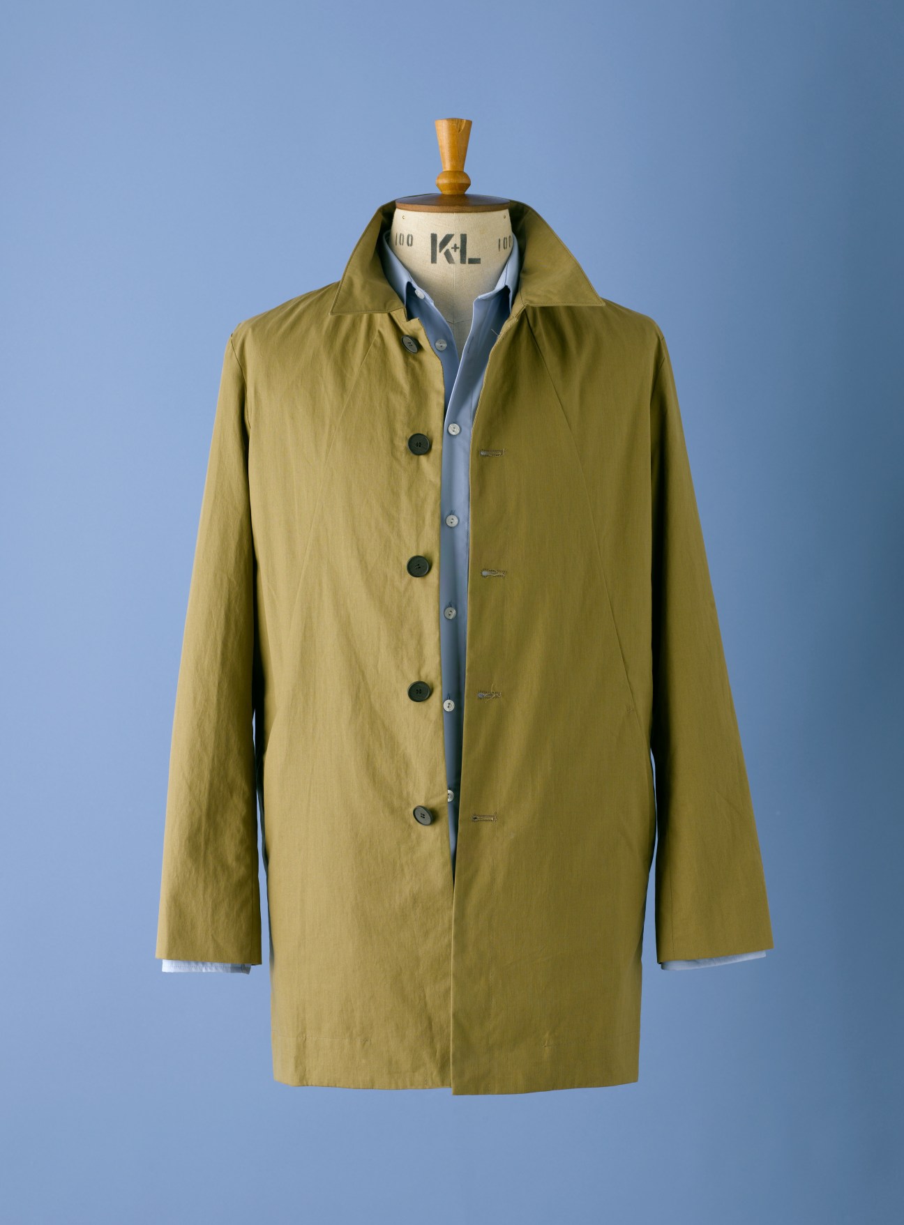 Yellow-green button-front coat on dress form against blue background.