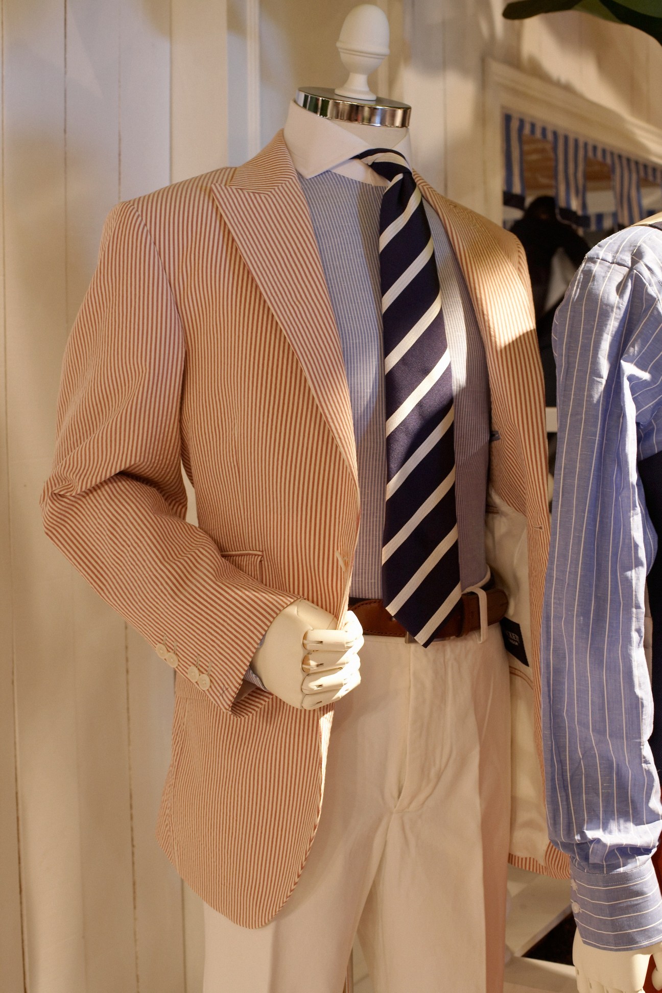 Mannequin dressed in a tan striped blazer with a navy and white striped tie by Hackett.