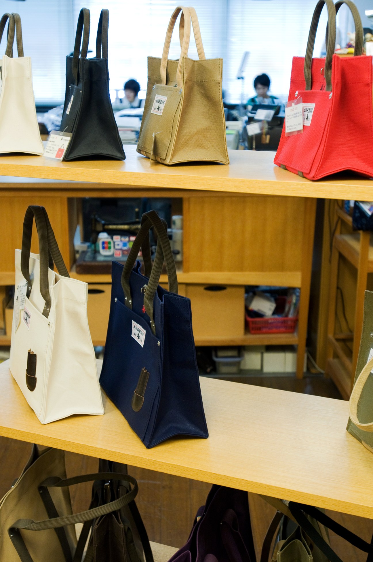 Inujirushi canvas tote bags in multiple colors displayed on wooden shelves in the shop.