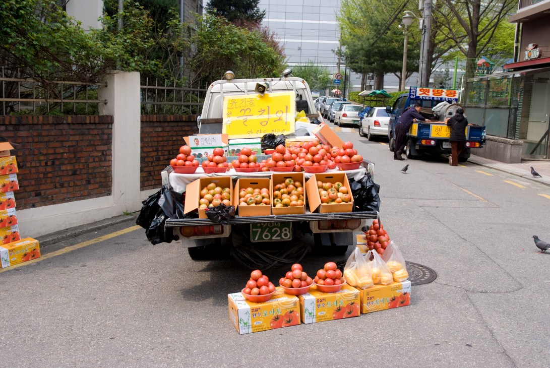 A mobile greengrocer truck loaded with fresh tomatoes and other produce on a Seoul street.