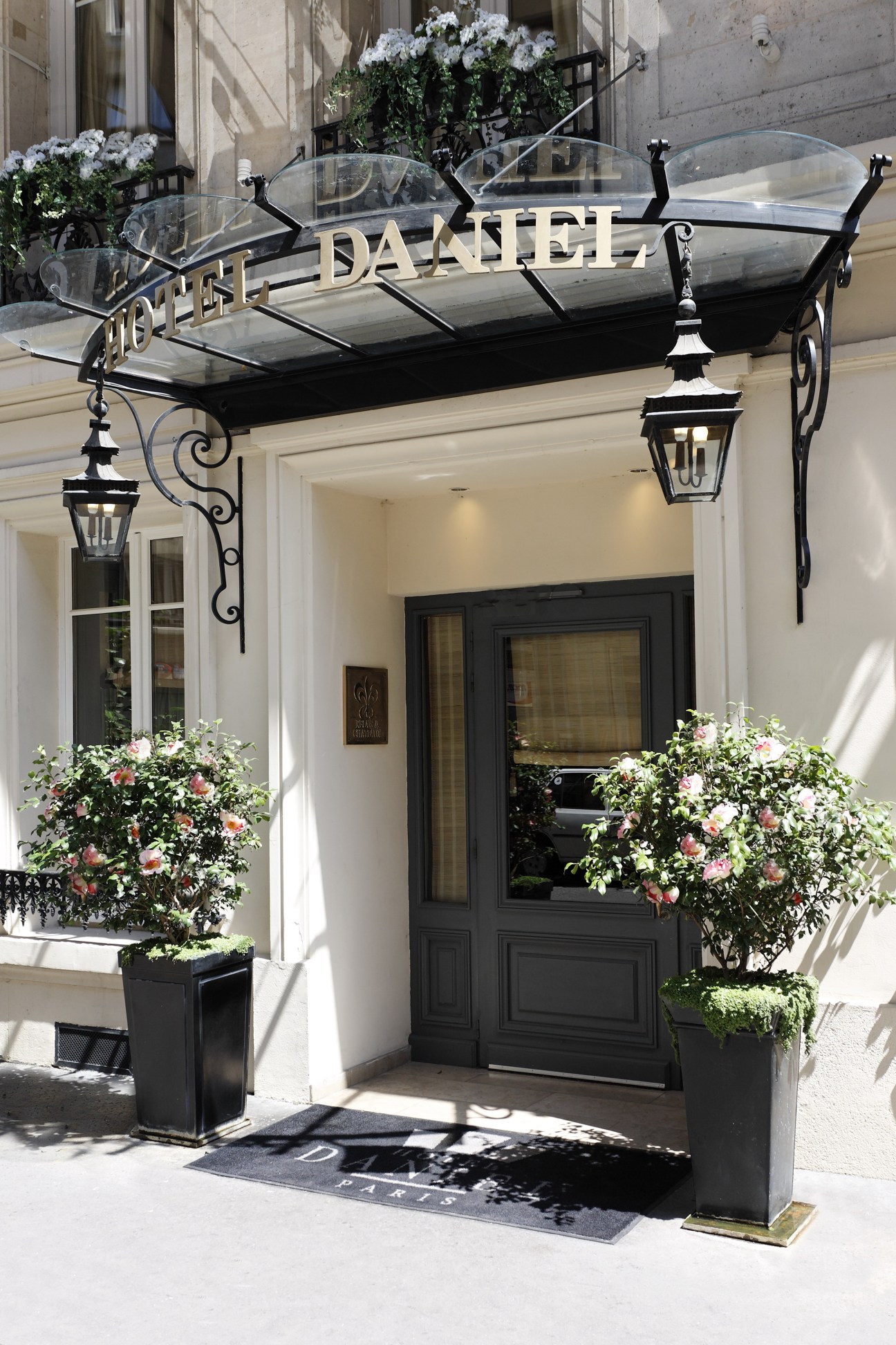 Hotel Daniel entrance in Paris with elegant black awning, flowering planters, and ornate lanterns.
