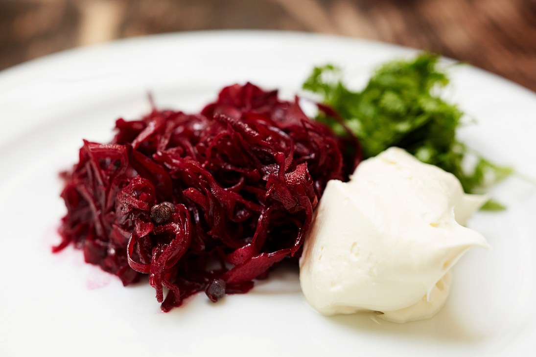 Shredded beetroot and red cabbage with a dollop of crème fraîche and garnish on a white plate.