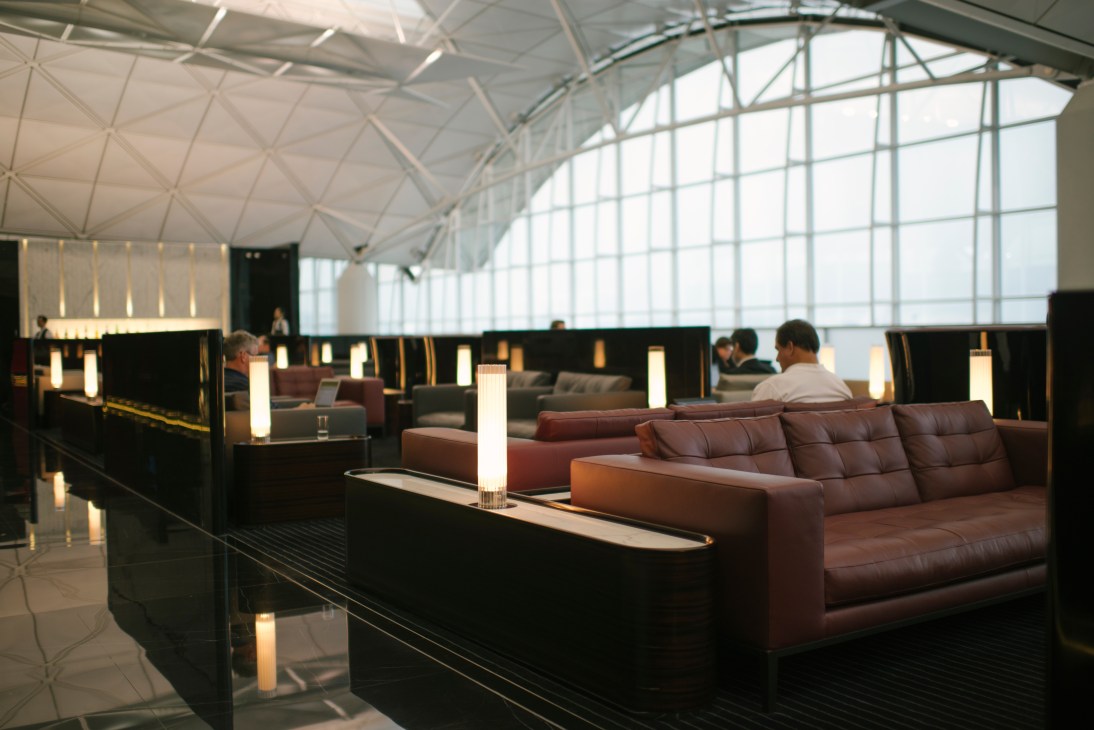 Modern airport lounge with burgundy leather seating, black partitions, and bright architectural ceiling