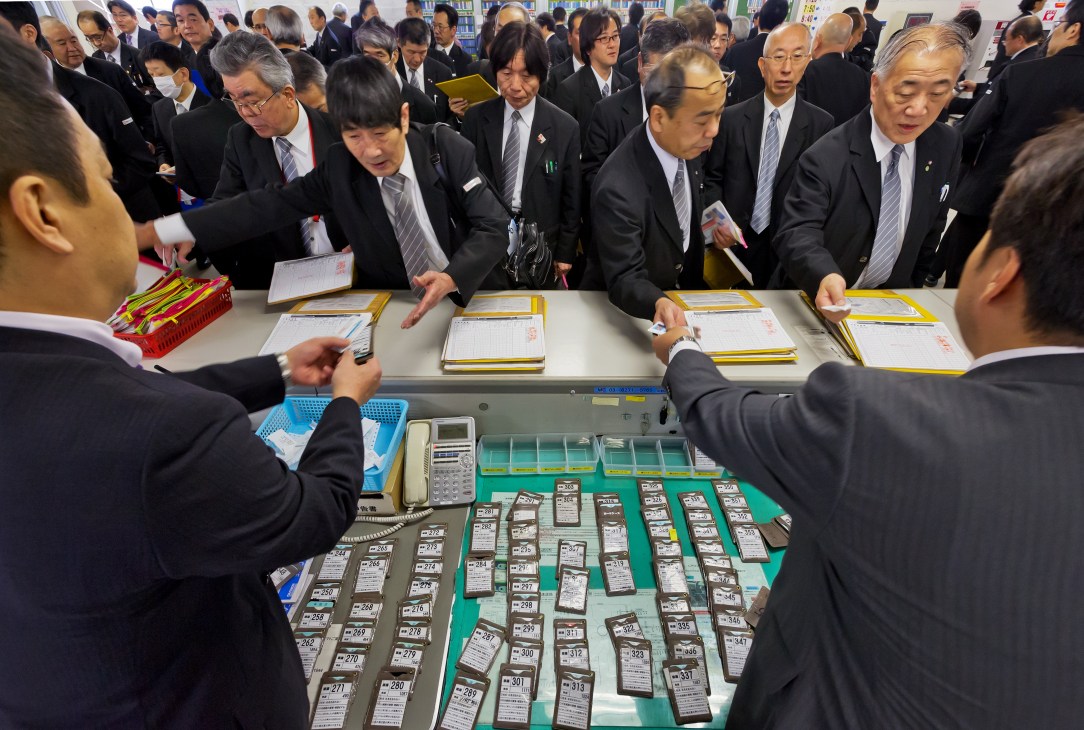 Nihon Kotsu taxi drivers in black suits and grey ties pick up their licences from a distribution table at the depot.