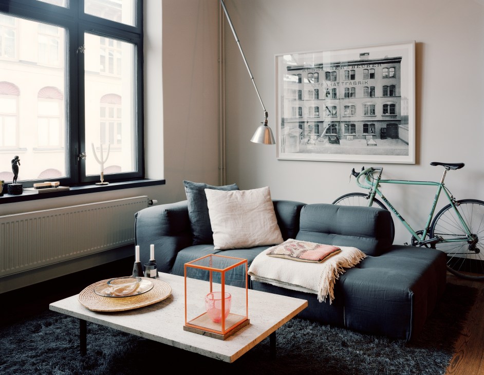 Andreas Martin-Löf's living room with a blue B&B Italia sofa by Patricia Urquiola, large windows, and a framed print of the original hat factory facade on the wall.