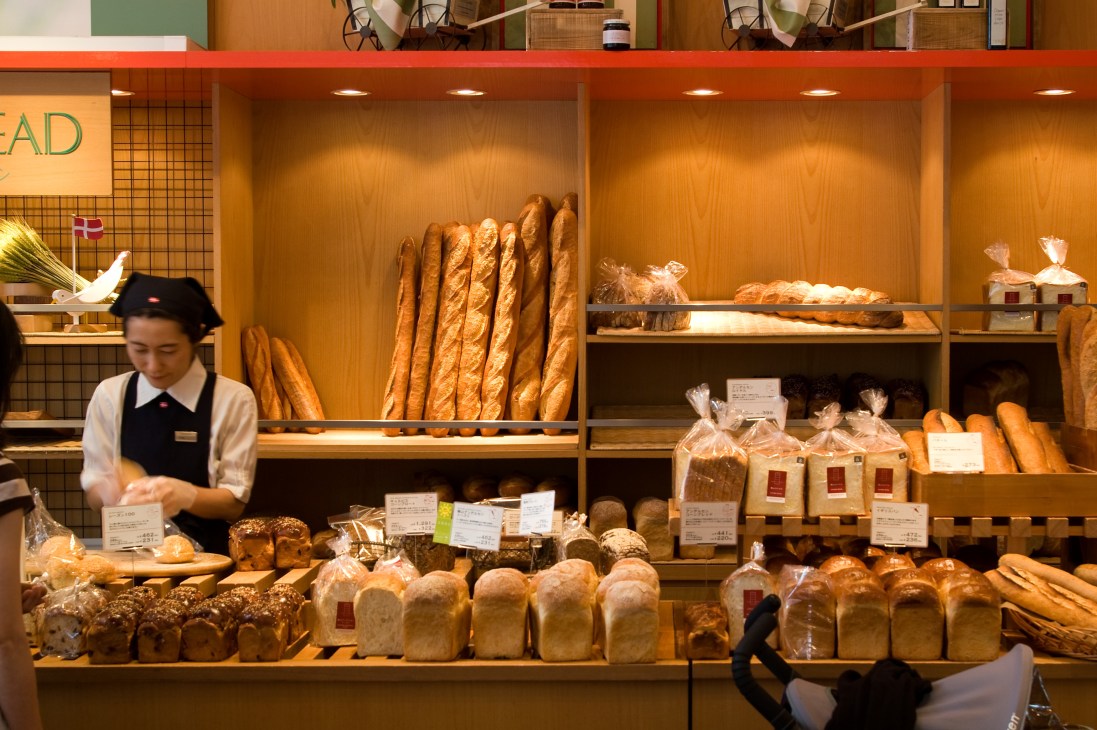 Andersen bakery display counter in Tokyo with staff arranging fresh bread and pastries behind illuminated wooden shelving.