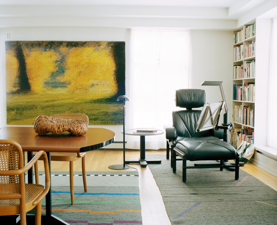 Modern living room with Diffrient-designed wooden table and chair, leather recliner, abstract artwork, and bookshelves.