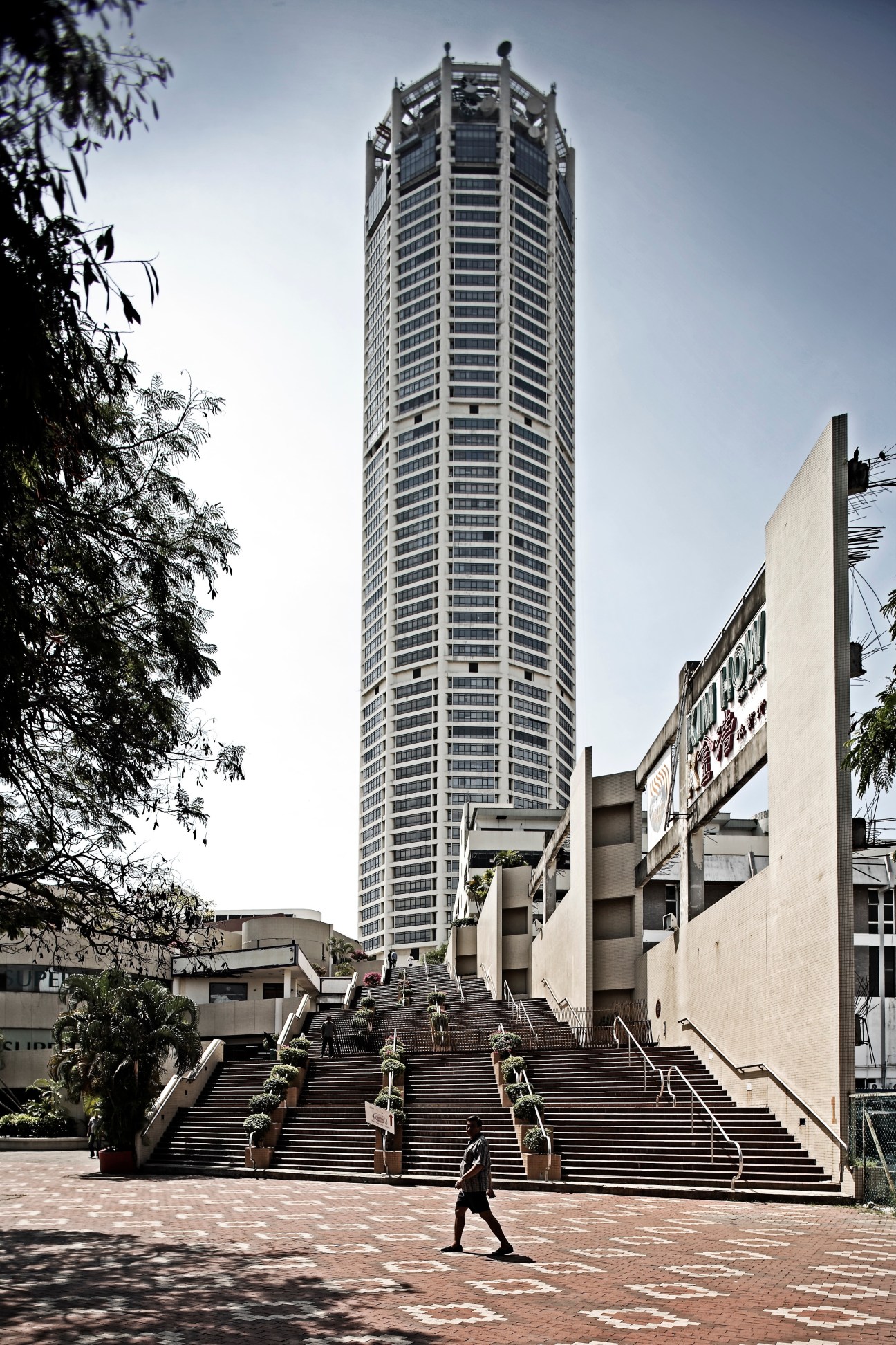The Komtar, a tall modernist tower rising above a plaza with stairs and colonial-era buildings in Penang.