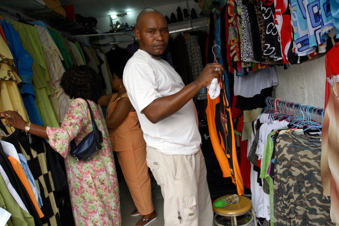 A Congolese man browses colorful fabrics and clothing hanging in a crowded market stall in Guangzhou.