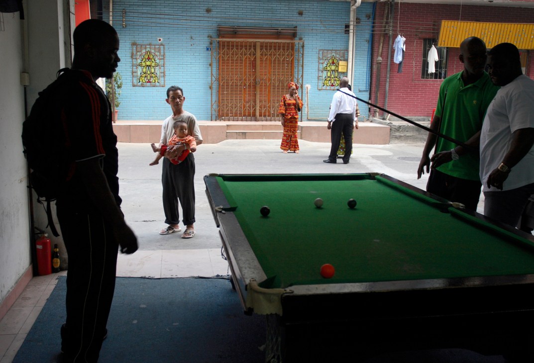 People playing pool at an outdoor bar in Guangzhou's Xiaobei area with colorful buildings in background.