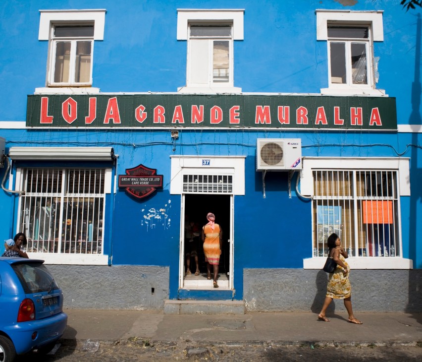 Bright blue storefront with red signage reading 'LOJA GRANDE MURALHA' and people on the street in Praia, Cape Verde.