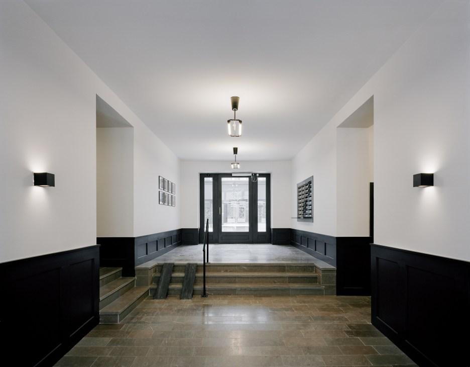 Minimalist entrance hall with polished concrete floor, white walls, black wainscoting, and modern pendant lights.