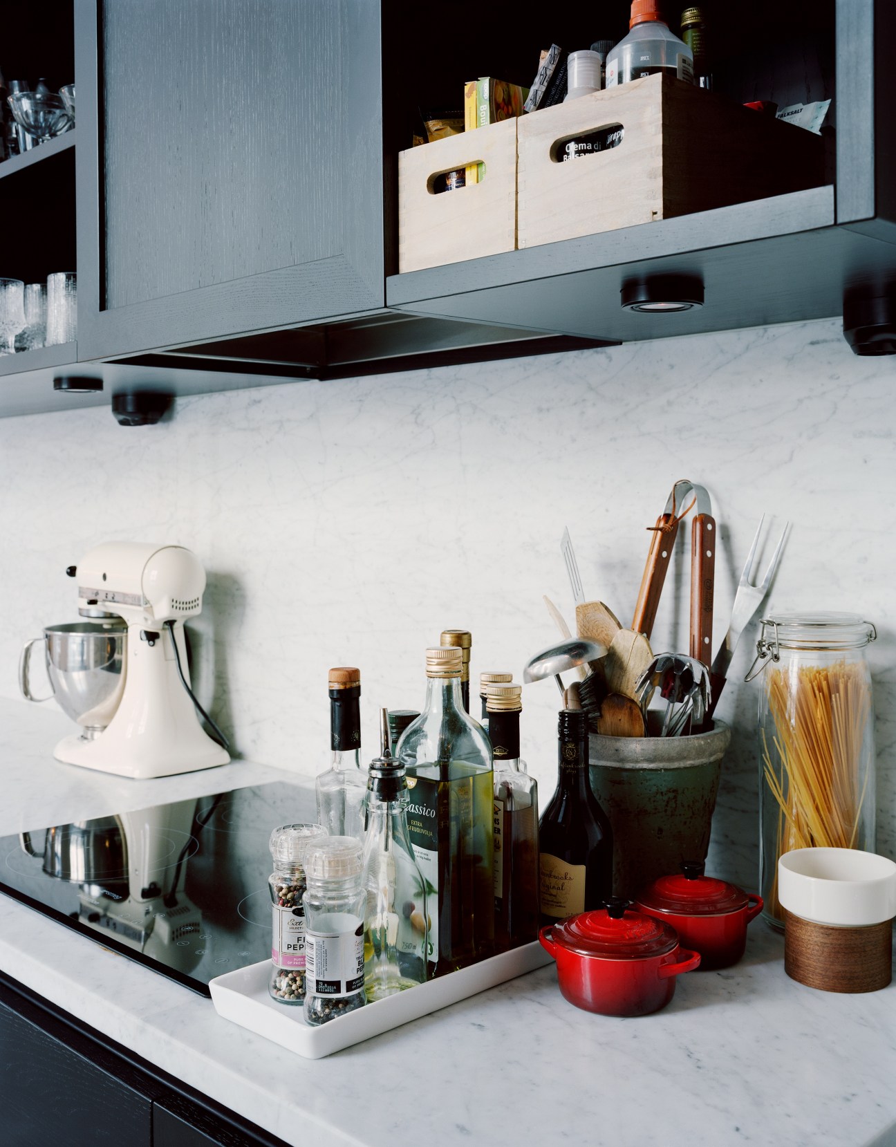 Modern kitchen counter with marble surface, cooking utensils, wine bottles, and red Le Creuset cookware.