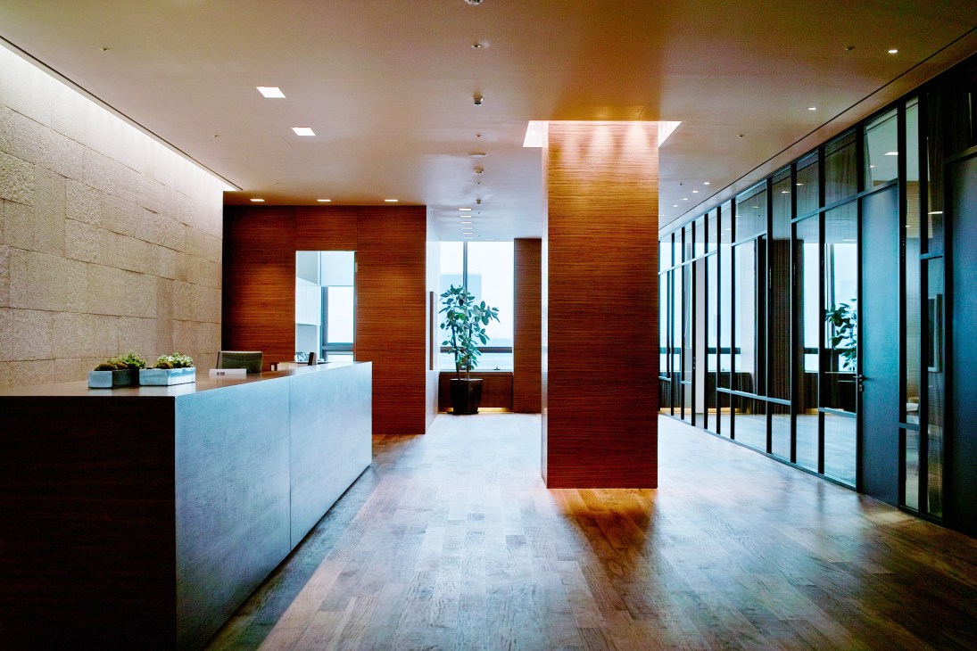 Modern office reception area with walnut wood columns, light stone walls, and traditional Cabreuva wood flooring.