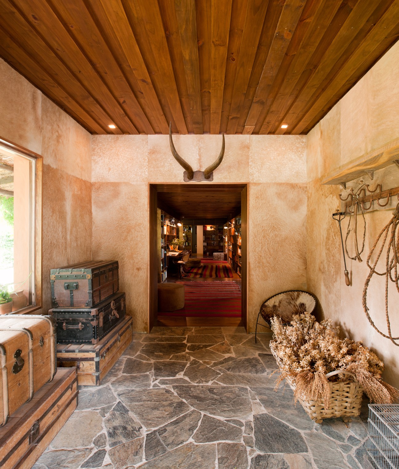 Rustic reception lobby with wooden ceiling, stone floor, vintage trunks and animal horns at Las Piedras Fasano hotel.