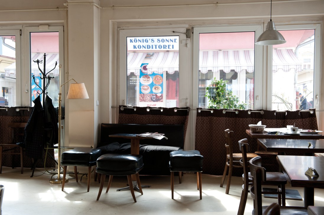 Madiani restaurant interior with black seating, large windows overlooking Karmelitermarkt, and vintage signage.