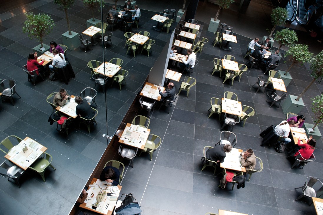 Overhead view of Neni im Zweiten restaurant with diners at tables with yellow chairs on dark floor.