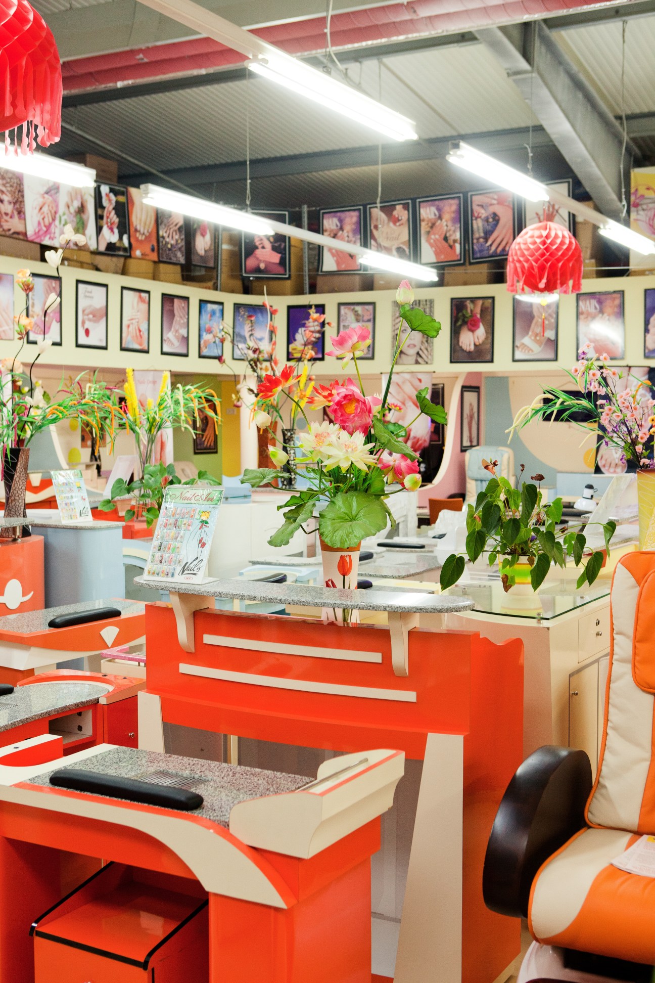 Bright nail salon interior with red and white furniture, flowering plants, and framed artwork on walls.
