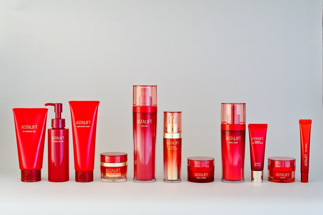 Astalift skincare products displayed in a line, featuring red and pink bottles and jars with gold accents.