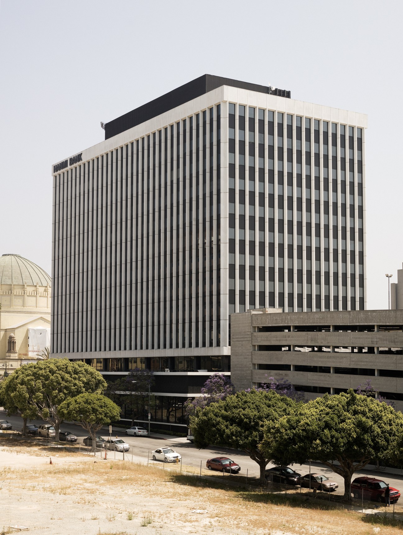 Modern office building with vertical ribbed facade and parking structure beside it in Los Angeles.