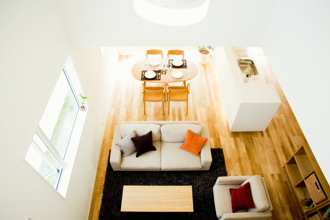 Overhead view of a Muji House interior showing minimalist open-plan living space with light wood flooring, neutral furniture, and large windows.