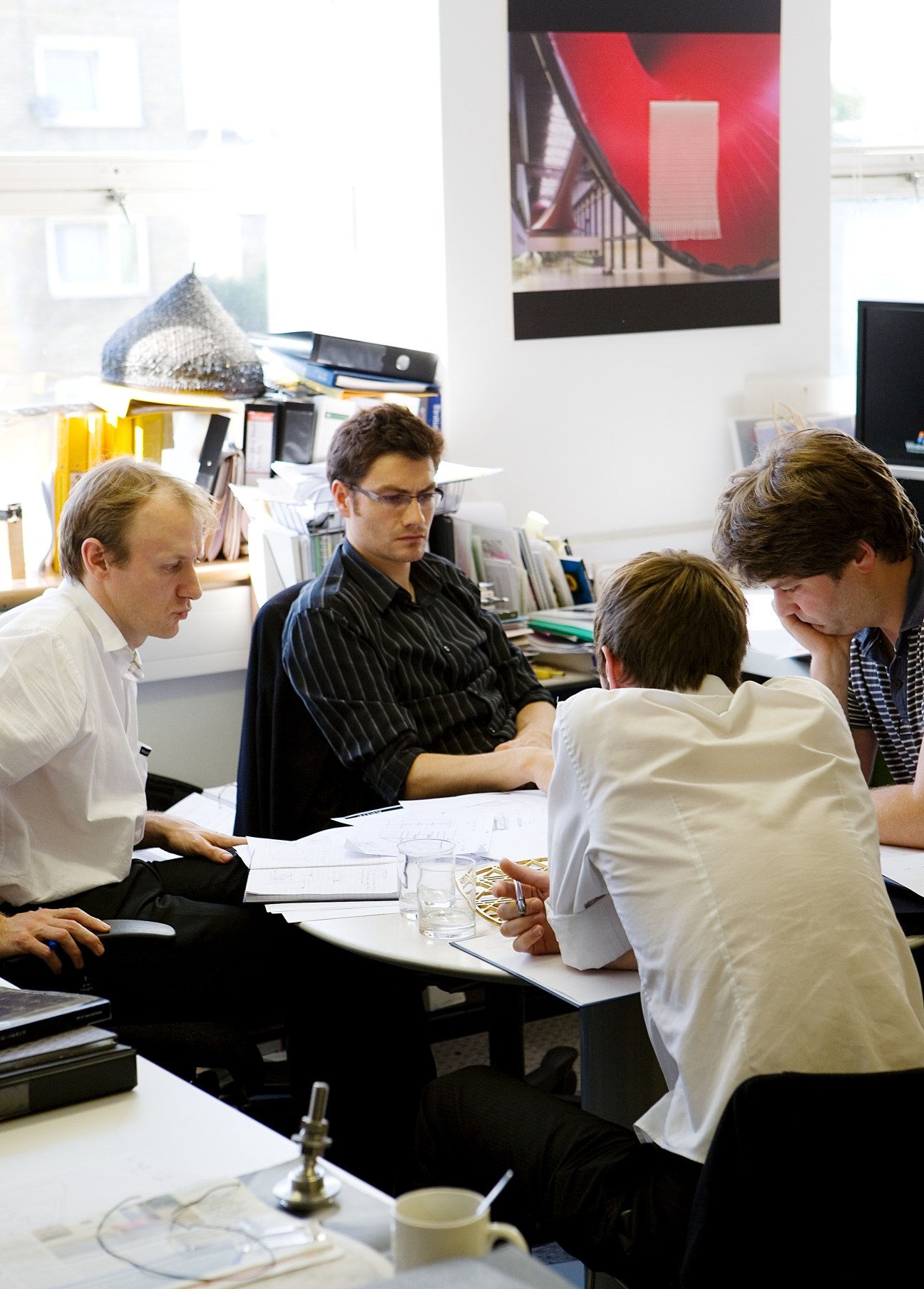 Four Arup staff members collaborate around a table reviewing project documents and models in a bright office.