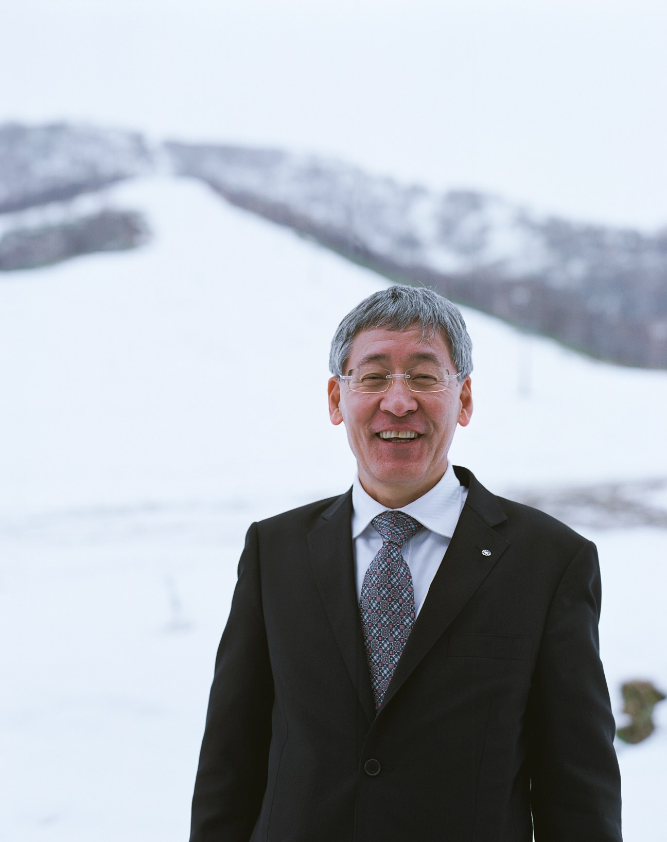 Mayor Kenya Katayama smiling in front of snowy ski slopes in Niseko.
