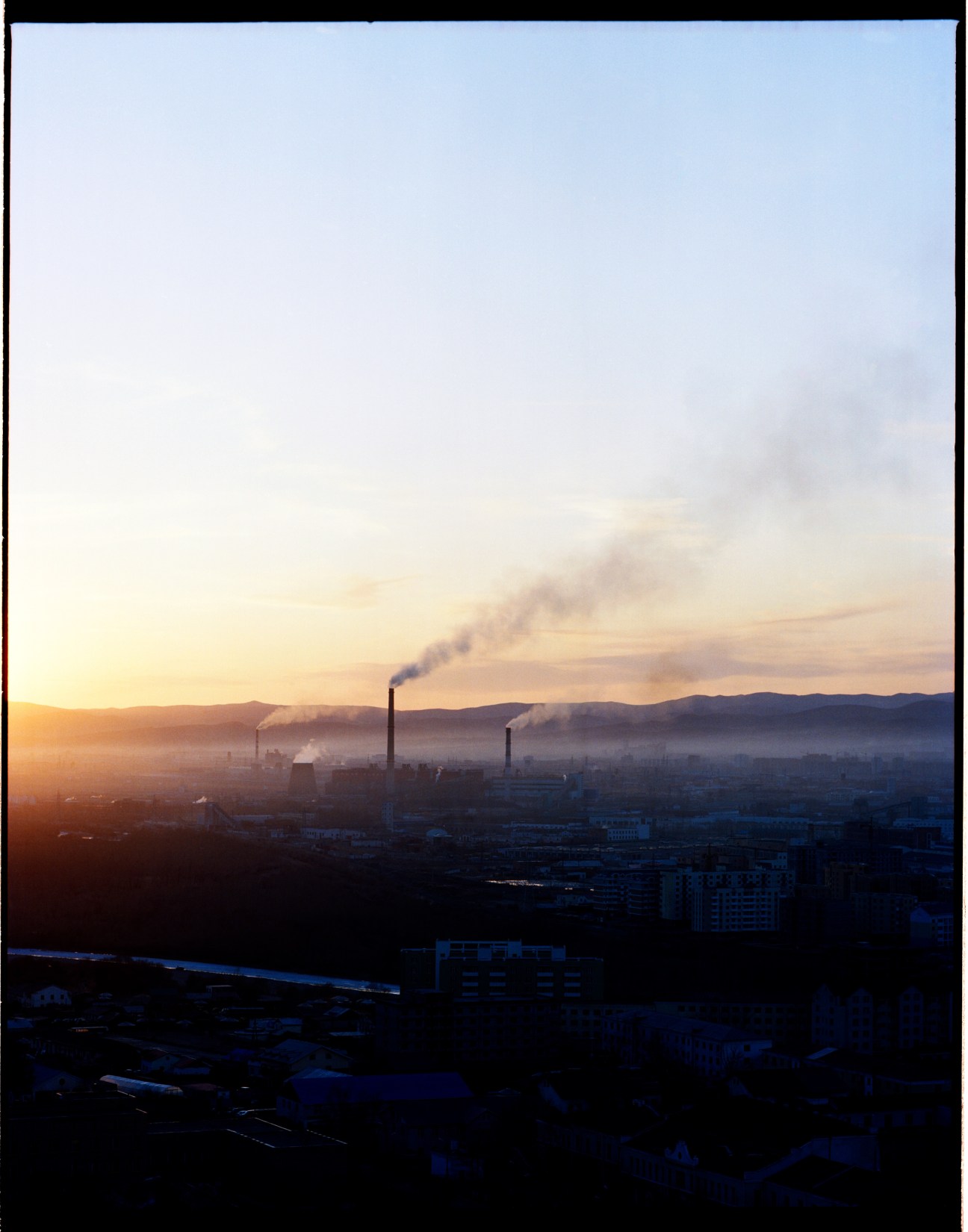Industrial power station with smoking chimneys at sunrise overlooking Ulan Bator's residential suburbs in a hazy valley.