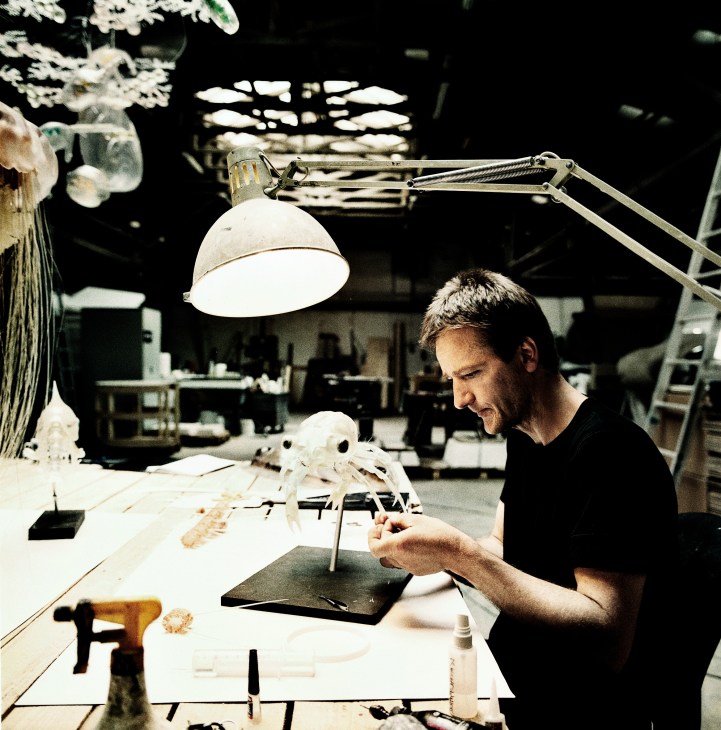 Esben Horn works on a detailed crab larvae model at his workbench under a desk lamp.
