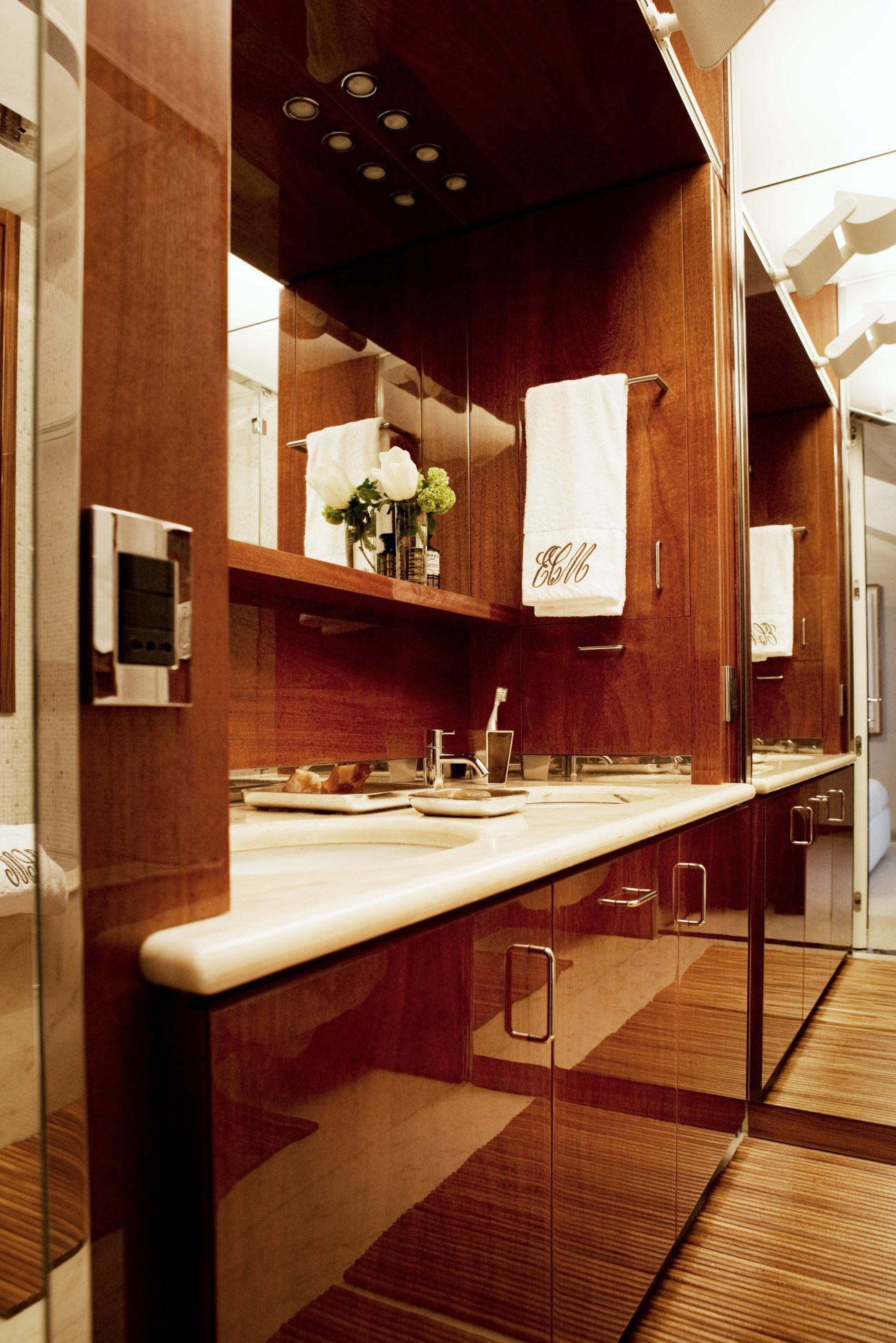 Modern bathroom with mahogany cabinetry, illuminated mirror, and natural light from square windows.
