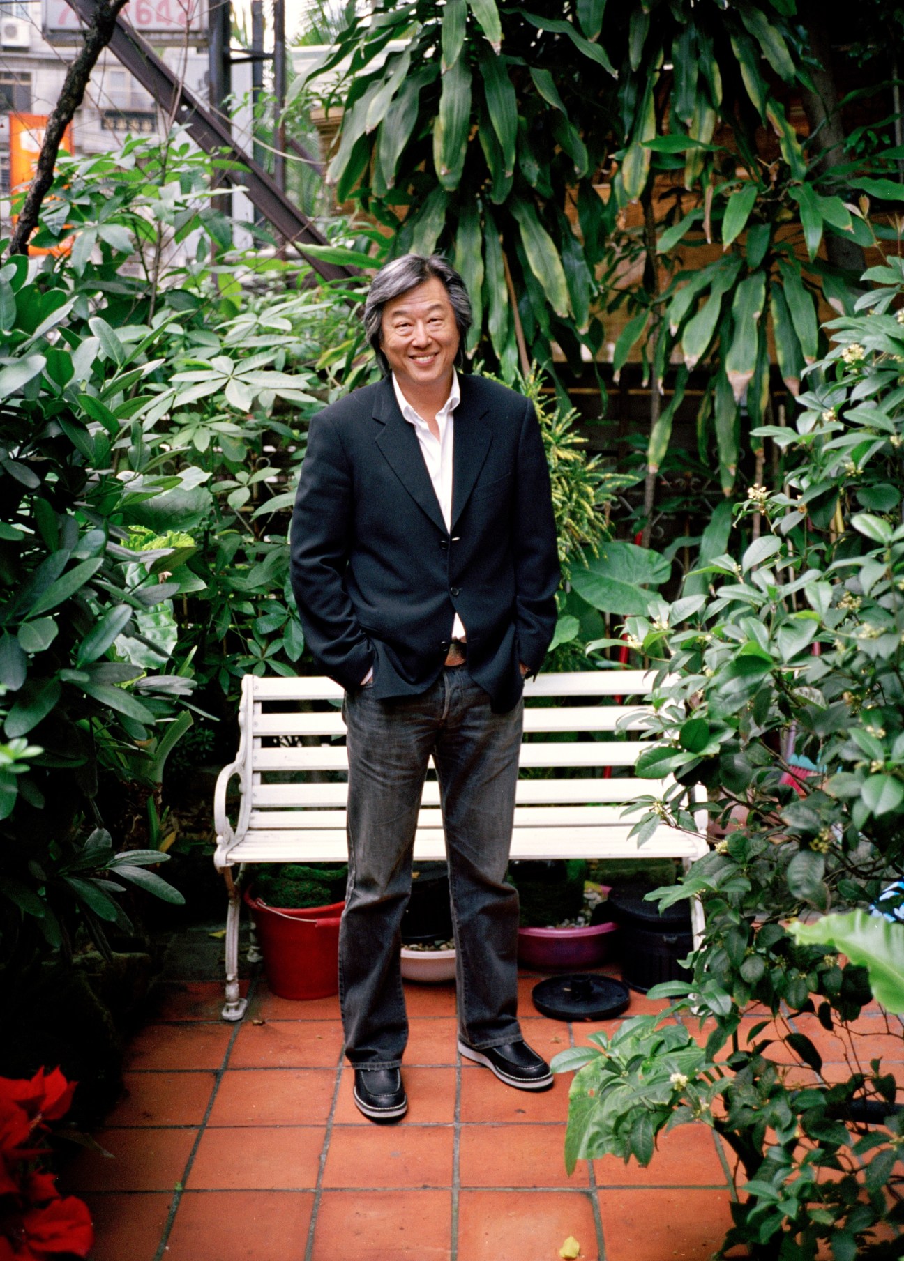 Wang Wei Chun stands in a lush garden setting wearing a dark blazer and jeans.